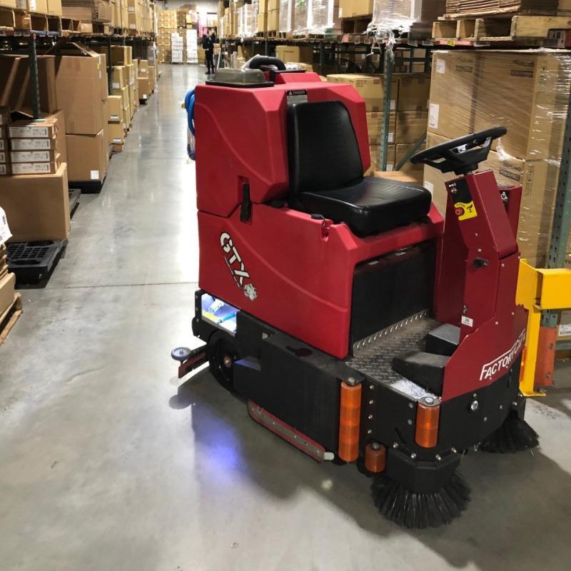 FactoryCat Ride On Floor Scrubbers GTX warehouse concrete - https://assets.factorycat.com/demoImages/2025/april/GTX-Ride On Floor Scrubbers-warehouse-concrete-Nashville-USA-829.jpg - 800 - 800 - 829 A FactoryCat GTX Ride On Floor Scrubber cleaning the concrete aisles of a warehouse in a Nashville, Tennessee contract manufacturer